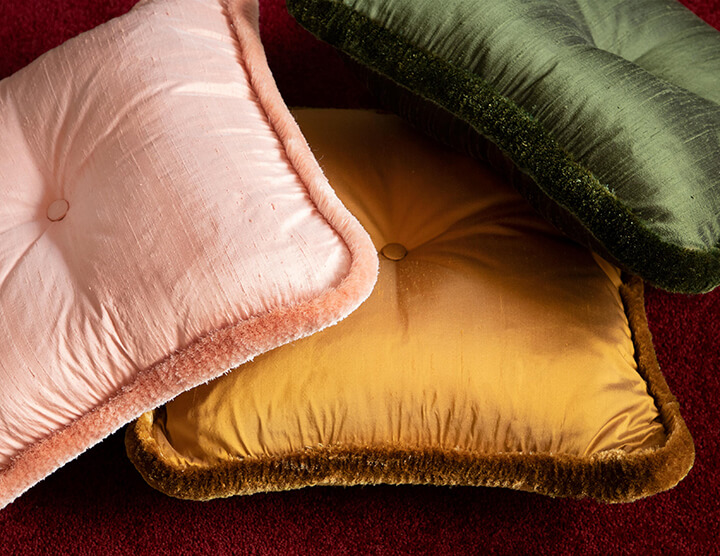 Pink, gold, and dark green raw silk pillows edged with plush silk brush fringe.